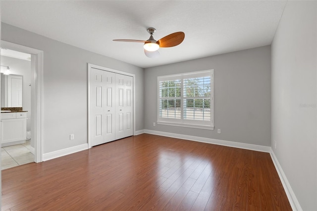 unfurnished bedroom with ensuite bath, wood-type flooring, ceiling fan, and a closet