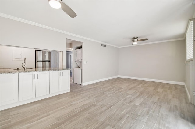 unfurnished living room with stacked washer and clothes dryer, crown molding, sink, ceiling fan, and light hardwood / wood-style floors