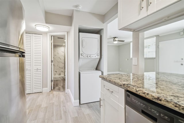 kitchen featuring dishwasher, white cabinetry, light stone countertops, and stacked washer / drying machine