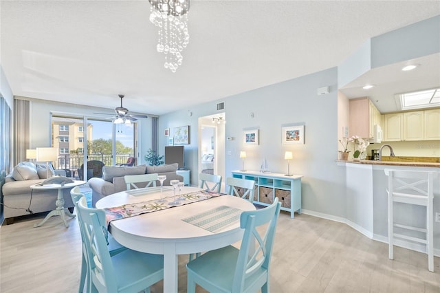 dining area featuring a textured ceiling, sink, light hardwood / wood-style floors, and ceiling fan with notable chandelier