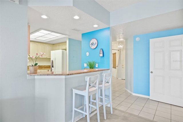 kitchen with white fridge with ice dispenser, kitchen peninsula, and light tile patterned floors