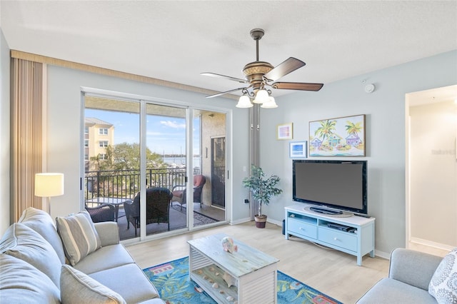 living room with baseboards, ceiling fan, a textured ceiling, and light wood finished floors