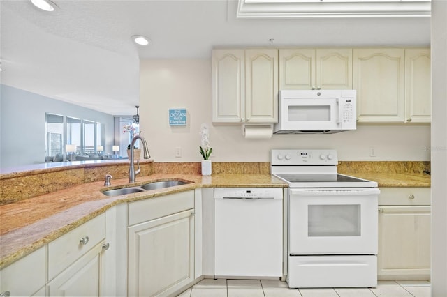 kitchen with light tile patterned floors, cream cabinets, a sink, light stone countertops, and white appliances