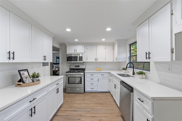 kitchen featuring white cabinets, sink, decorative backsplash, light wood-type flooring, and appliances with stainless steel finishes