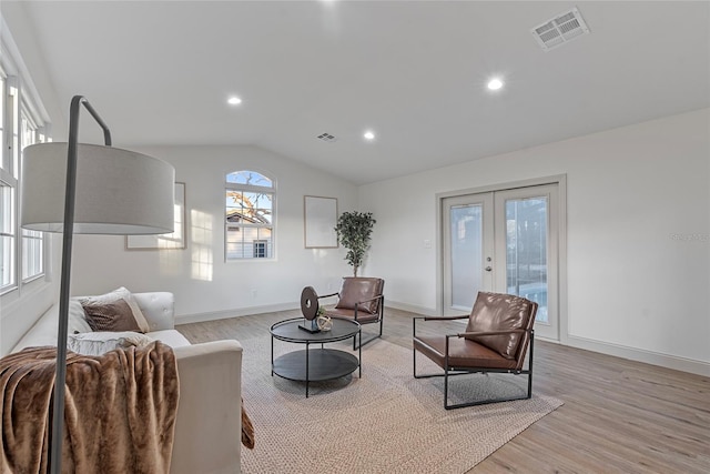 living room featuring vaulted ceiling, light wood-type flooring, and french doors