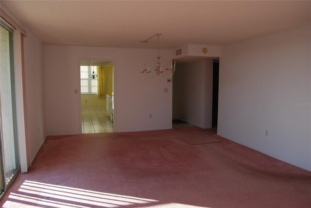 carpeted spare room featuring an inviting chandelier