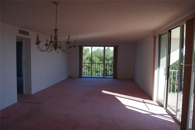 spare room with carpet flooring, a textured ceiling, and a notable chandelier