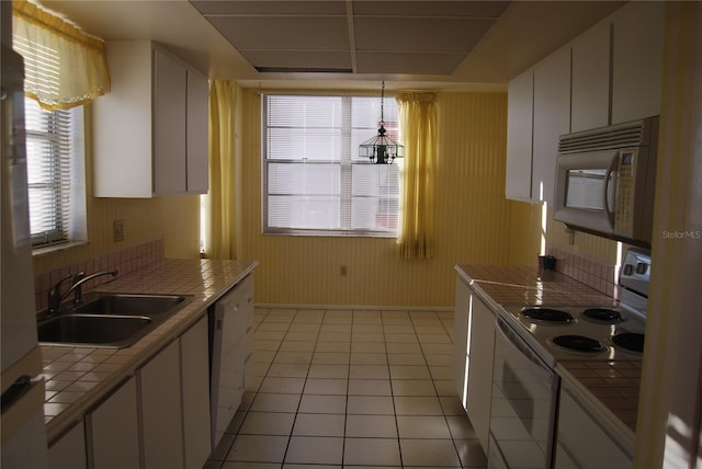 kitchen featuring white appliances, sink, decorative light fixtures, white cabinetry, and tile counters