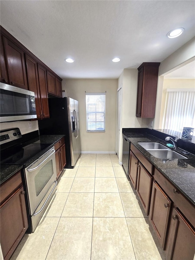 kitchen featuring dark stone countertops, sink, light tile patterned floors, and stainless steel appliances