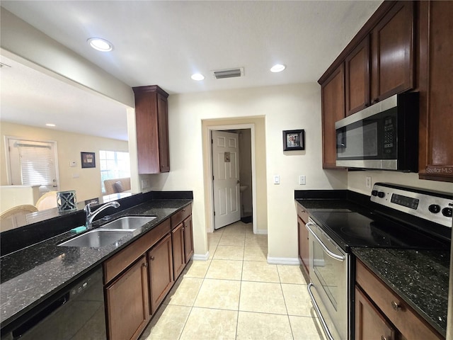 kitchen with light tile patterned flooring, appliances with stainless steel finishes, dark stone countertops, and sink