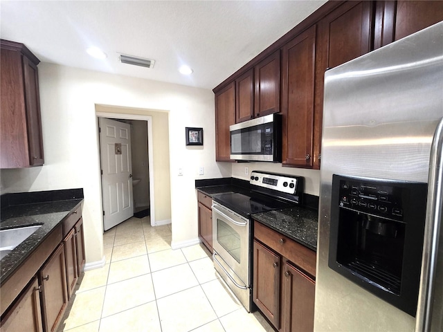 kitchen with dark stone countertops, dark brown cabinets, light tile patterned flooring, and stainless steel appliances