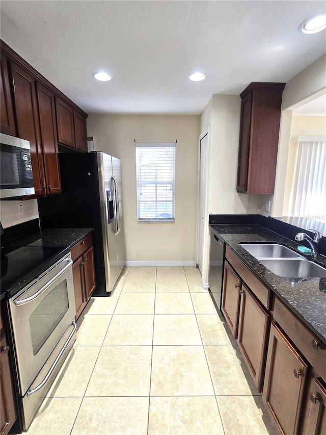 kitchen featuring light tile patterned floors, stainless steel appliances, dark stone countertops, and sink