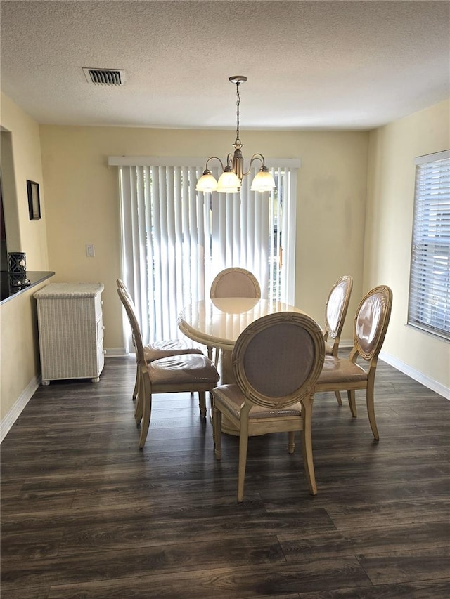 dining space with dark wood-type flooring, a textured ceiling, and an inviting chandelier