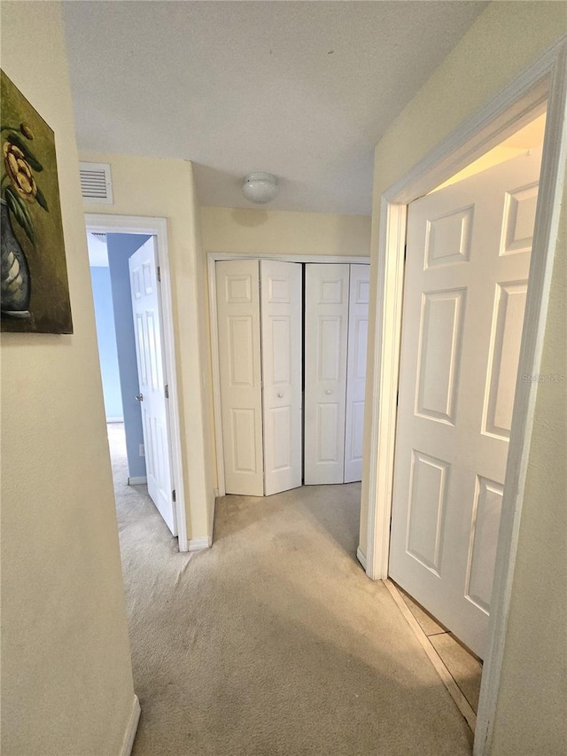 hallway with light carpet and a textured ceiling