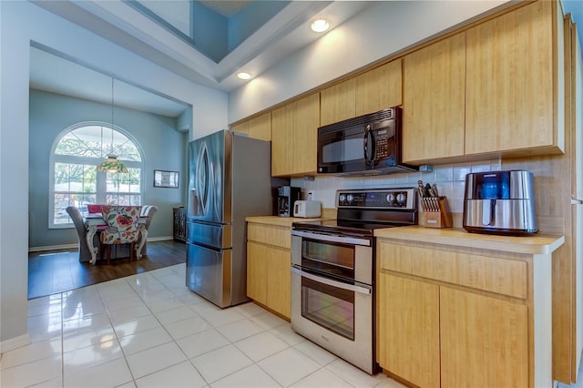 kitchen with backsplash, light brown cabinetry, light tile patterned flooring, and stainless steel appliances