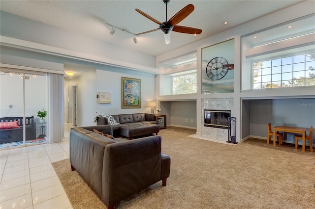 tiled living room with a high end fireplace, rail lighting, a textured ceiling, ceiling fan, and a high ceiling