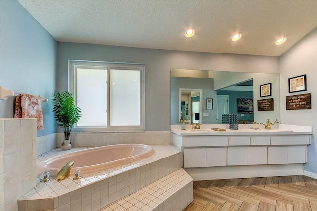 bathroom with vanity, a textured ceiling, tiled bath, and parquet floors