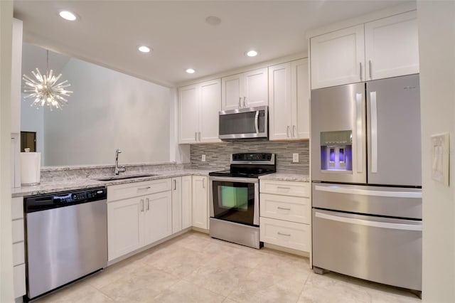 kitchen with light stone countertops, stainless steel appliances, sink, a notable chandelier, and white cabinetry