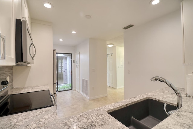 kitchen featuring light stone countertops, backsplash, stainless steel appliances, sink, and white cabinetry