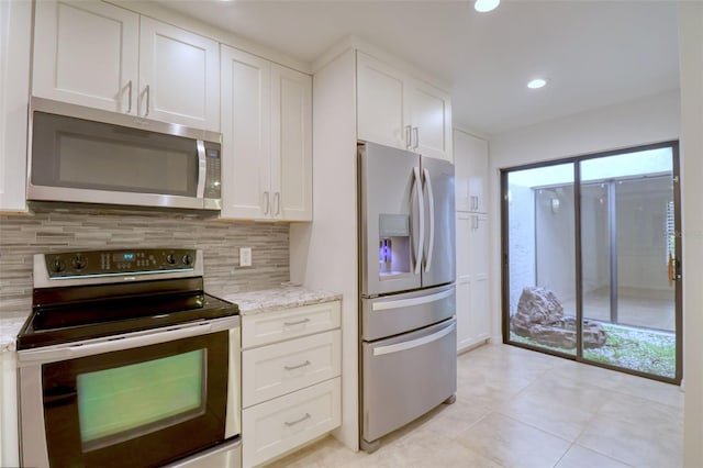 kitchen with light stone countertops, appliances with stainless steel finishes, decorative backsplash, light tile patterned floors, and white cabinetry