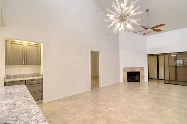 unfurnished living room with ceiling fan with notable chandelier, high vaulted ceiling, and a tiled fireplace