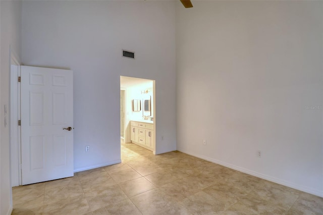 unfurnished bedroom featuring ceiling fan, a high ceiling, and ensuite bath