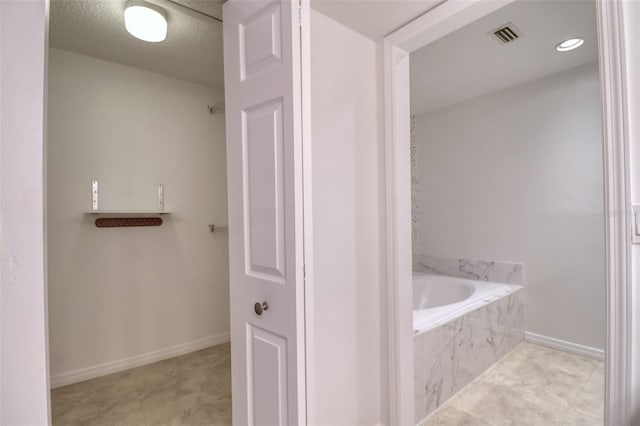 bathroom with tiled tub and a textured ceiling