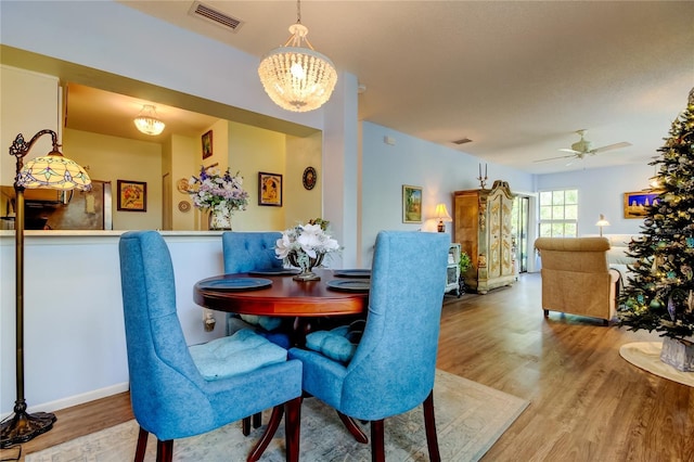 dining area with ceiling fan with notable chandelier and hardwood / wood-style flooring