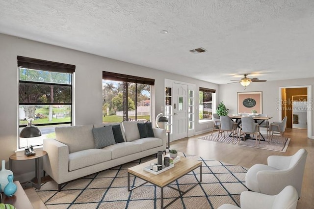 living room featuring a wealth of natural light, ceiling fan, light hardwood / wood-style floors, and a textured ceiling