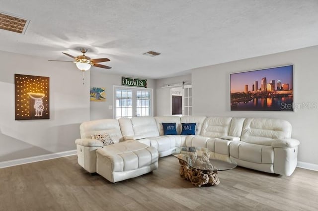 living room featuring ceiling fan, wood-type flooring, a textured ceiling, and french doors