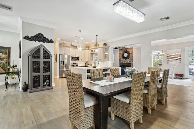 dining room featuring light hardwood / wood-style floors, an inviting chandelier, ornamental molding, and a brick fireplace