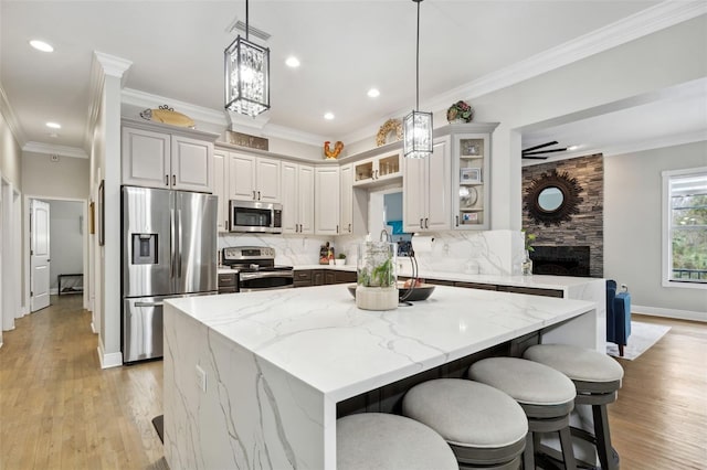 kitchen with light stone counters, light wood-type flooring, decorative backsplash, appliances with stainless steel finishes, and ornamental molding