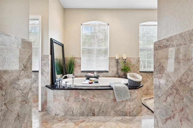 bathroom with a relaxing tiled tub, a healthy amount of sunlight, and tile walls