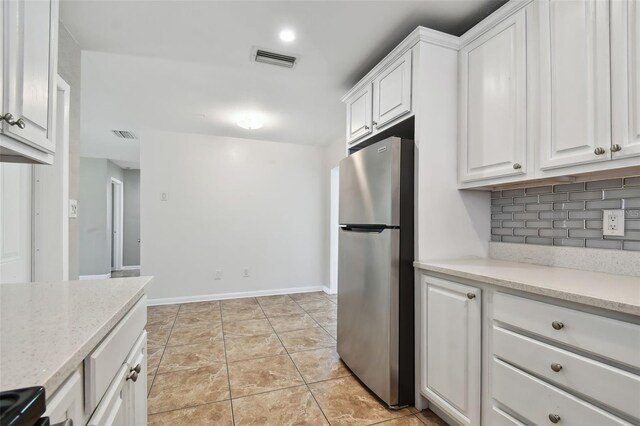 kitchen featuring decorative backsplash, light stone counters, white cabinets, stainless steel refrigerator, and light tile patterned flooring