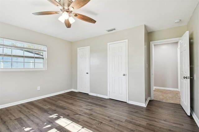 unfurnished bedroom featuring dark hardwood / wood-style floors, ceiling fan, and multiple closets