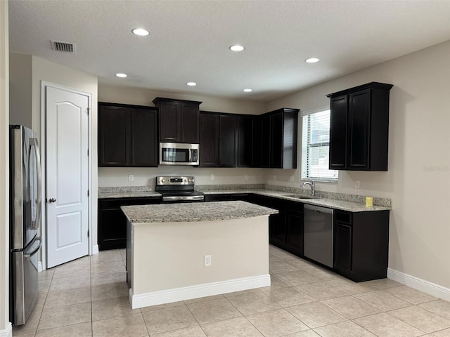 kitchen with light stone countertops, sink, a center island, a textured ceiling, and appliances with stainless steel finishes