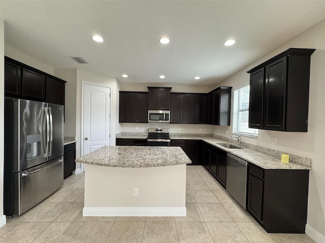 kitchen with sink, stainless steel appliances, light stone counters, a textured ceiling, and a kitchen island