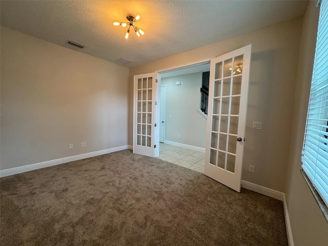 carpeted spare room featuring a chandelier, french doors, a textured ceiling, and a wealth of natural light