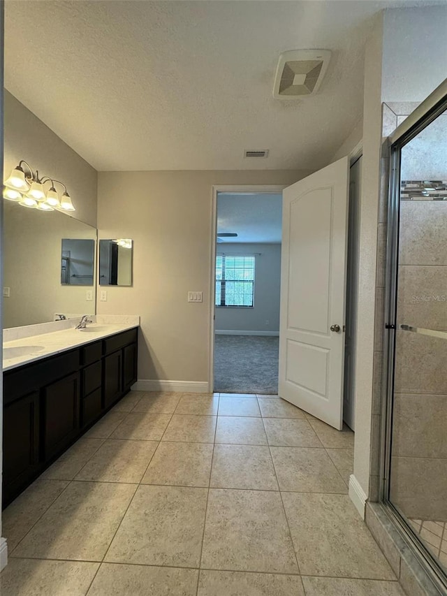 bathroom with tile patterned flooring, vanity, a shower with door, and a textured ceiling