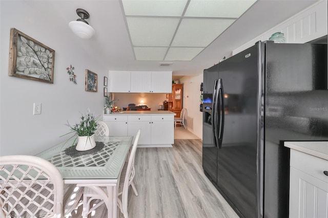 kitchen featuring white cabinetry, black fridge, a drop ceiling, and light hardwood / wood-style flooring