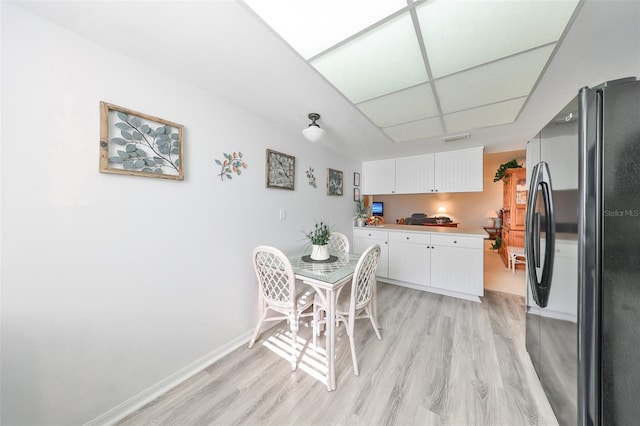 kitchen with white cabinetry, black fridge, and light hardwood / wood-style flooring