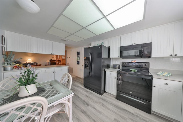 kitchen with light hardwood / wood-style flooring, white cabinets, and black appliances