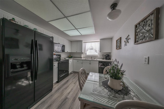 kitchen with a drop ceiling, black appliances, sink, light hardwood / wood-style floors, and white cabinetry