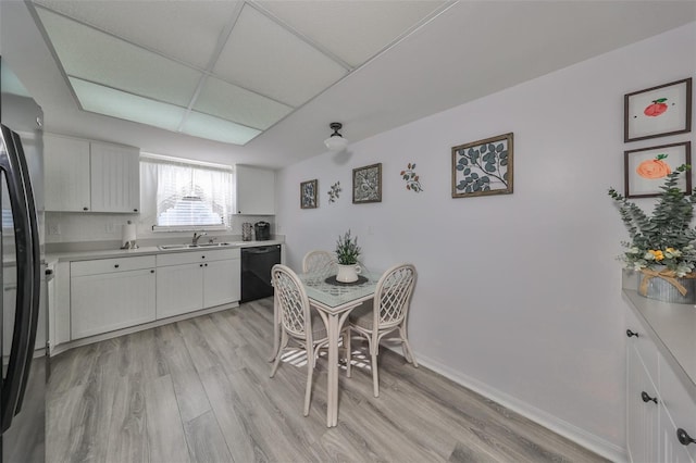 kitchen featuring white cabinets, sink, light wood-type flooring, black dishwasher, and stainless steel refrigerator