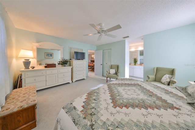 bedroom featuring ensuite bathroom, a textured ceiling, light colored carpet, ceiling fan, and a closet