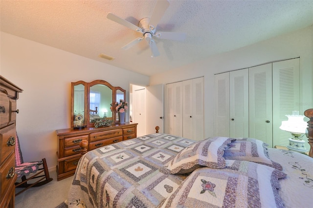 bedroom with two closets, ceiling fan, light colored carpet, and a textured ceiling