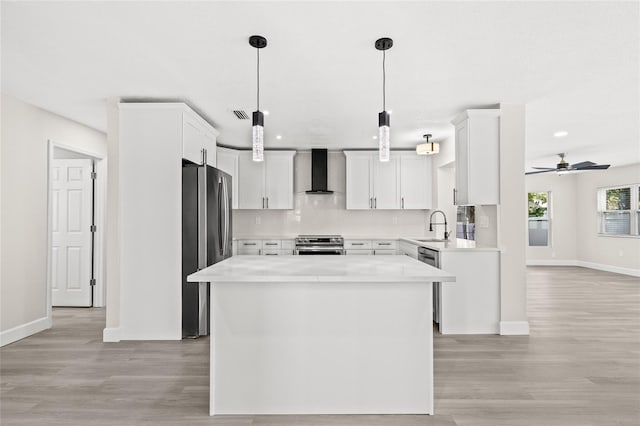 kitchen featuring white cabinets, a center island, wall chimney range hood, and stainless steel appliances