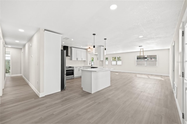 kitchen with appliances with stainless steel finishes, wall chimney range hood, decorative light fixtures, light hardwood / wood-style flooring, and white cabinetry