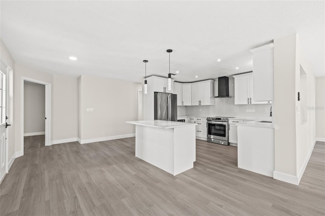 kitchen featuring wall chimney range hood, hanging light fixtures, light wood-type flooring, appliances with stainless steel finishes, and a kitchen island