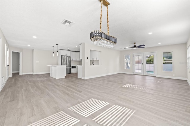 unfurnished living room with a textured ceiling, light hardwood / wood-style flooring, ceiling fan with notable chandelier, and french doors